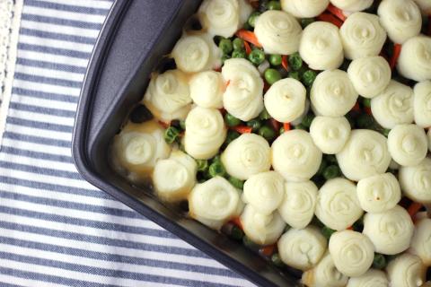 pan of cooked turkey, gravy, and vegetables topped with mashed potatoes