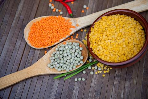 Spoons full of red and green lentils, next to a bowl of yellow lentils