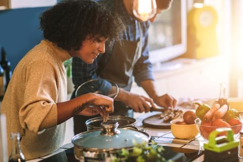 two people making food in kitchen. One is chopping vegetables and the other is stirring a pot. 