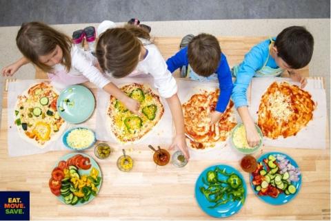 Four kids add different vegetable toppings to their own pizzas. 