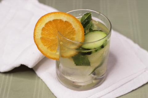 Glass of water with cucumber, mint and orange slices.