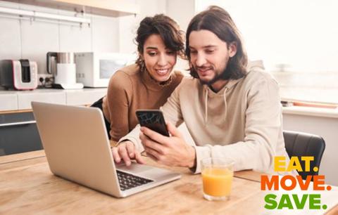 two people sitting at a table looking at a laptop and smart phone