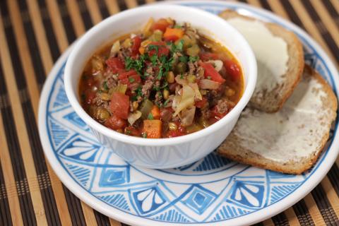 white bowl of venison cabbage lentil soup with buttered bread on the side