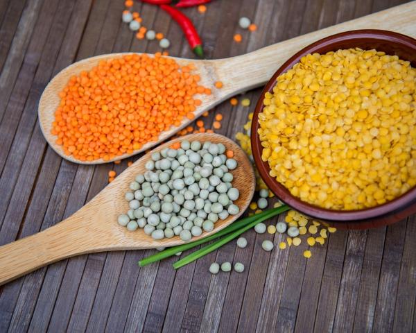 Spoons full of red and green lentils, next to a bowl of yellow lentils