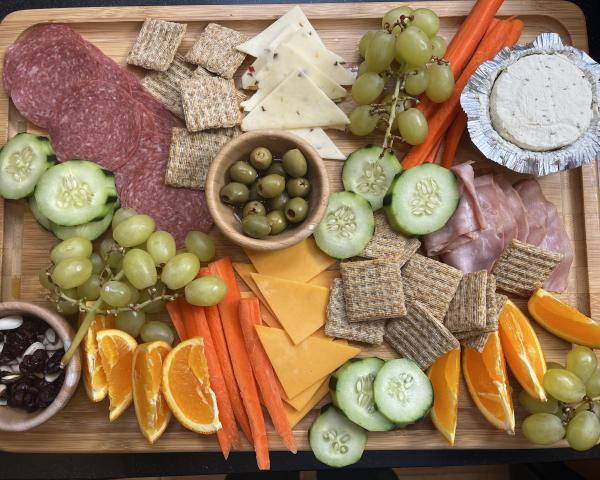 A charcuterie board with olives, cheese, meats, carrots, cucumbers, fruit, and crackers