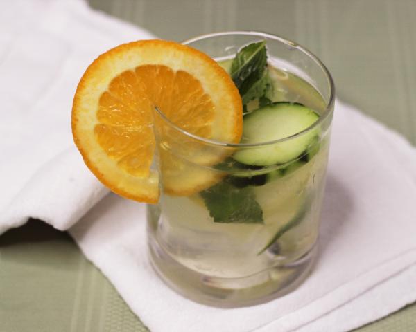 Glass of water with cucumber, mint and orange slices.