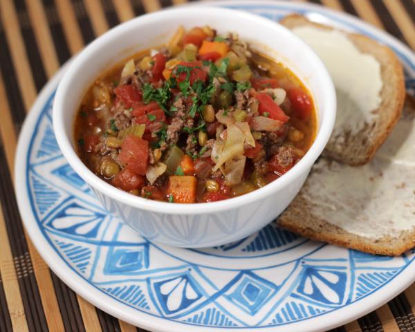 white bowl of venison cabbage lentil soup with buttered bread on the side