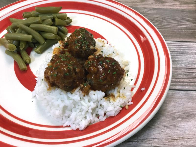 three meatballs in sauce over white rice on a white and red striped plate, green beans on side