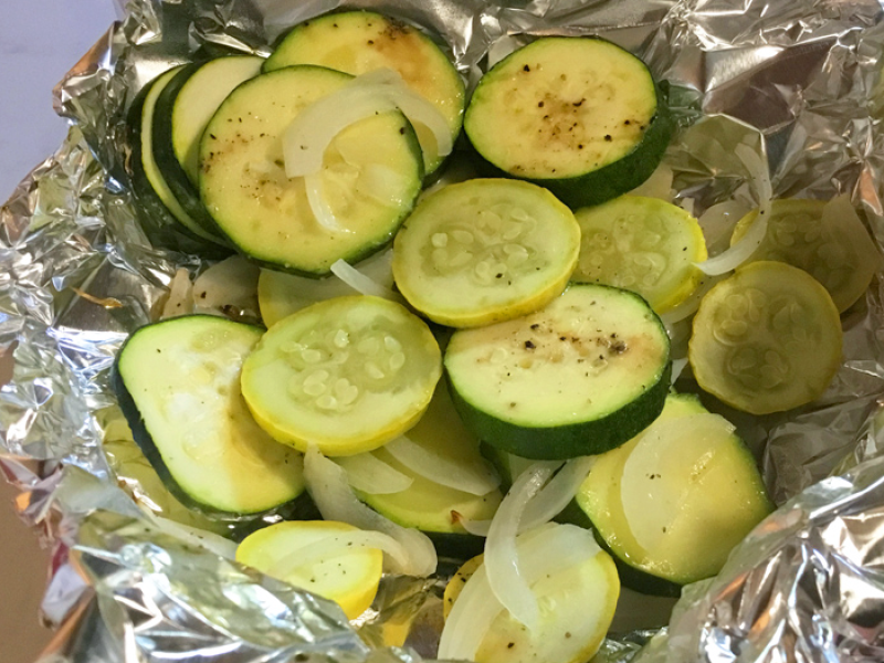 sliced zucchini and yellow squash in a foil packet with onions