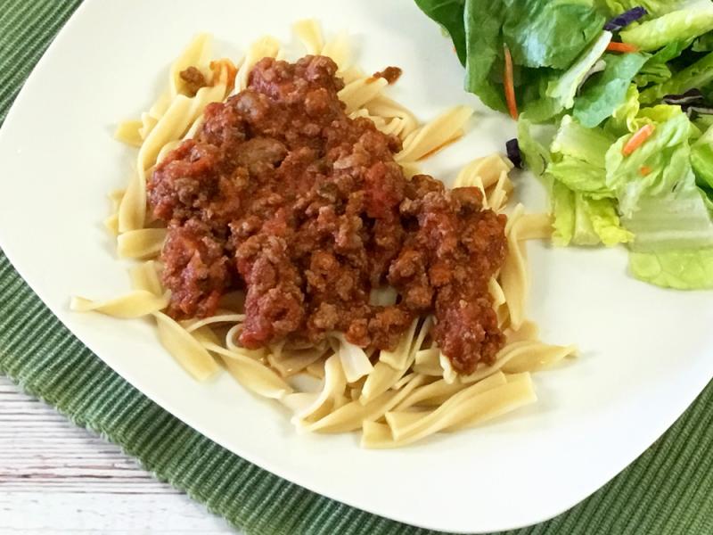 Plate of noodles with tomato meat sauce on top and mixed green salad on the side