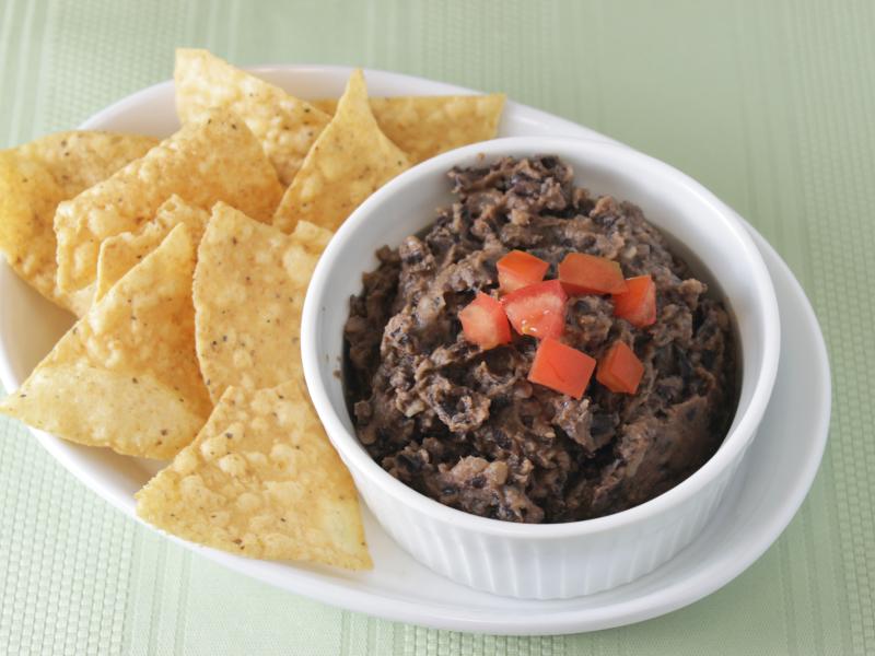 black bean dip in white bowl topped with diced tomato with tortilla chips on side