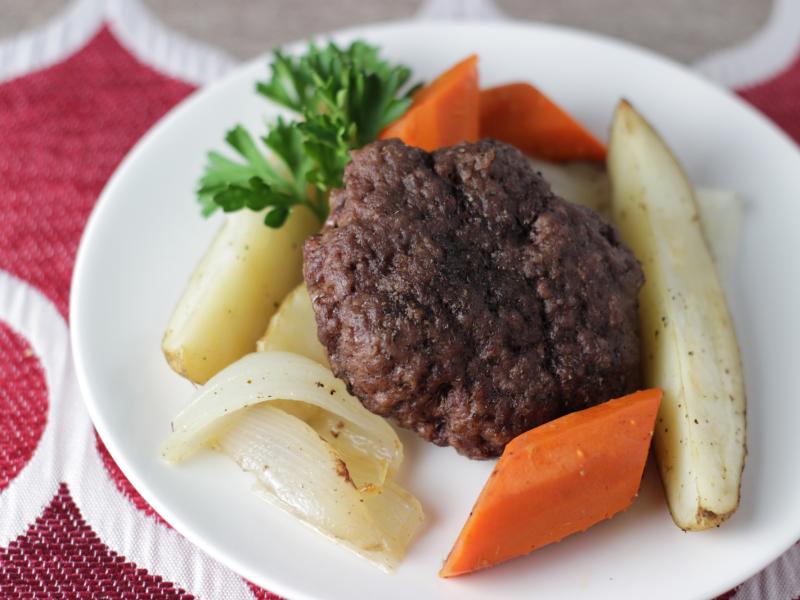 white plate with cooked beef burger patty surrounded by potato wedges, carrots, and onions