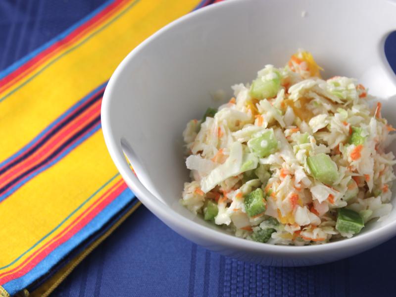 white bowl of coleslaw with cabbage, celery, orange segments, and green peppers