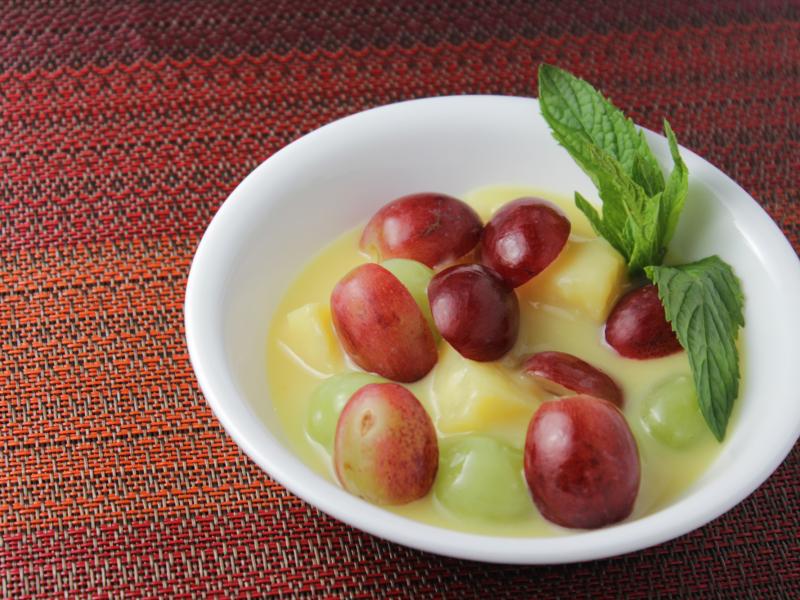 white dish with vanilla pudding, grapes, sliced bananas, pineapple topped with sliced red grapes