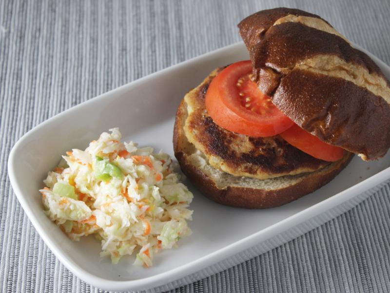 tuna patty topped with tomato on pretzel bun with side of coleslaw