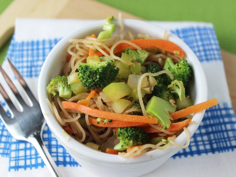 white bowl with broccoli, carrots, and other veggies mixed with noodles