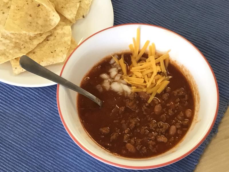 bowl of venison chili topped with cheese in a white bowl with tortilla chips on the side