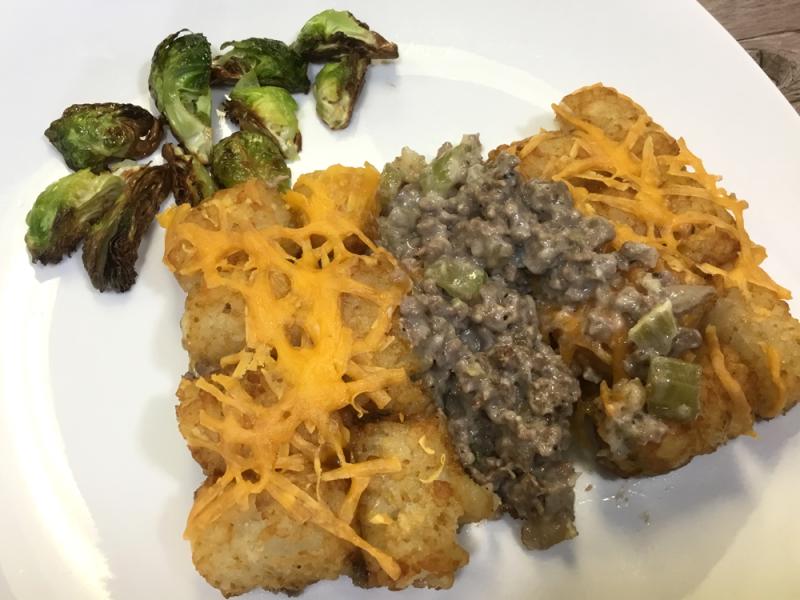 venison tator tot casserole topped with cheddar cheese on white plate with side of brussels sprouts