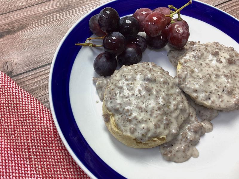 two half-biscuits covered in venison white gravy on a white plate with grapes on the side