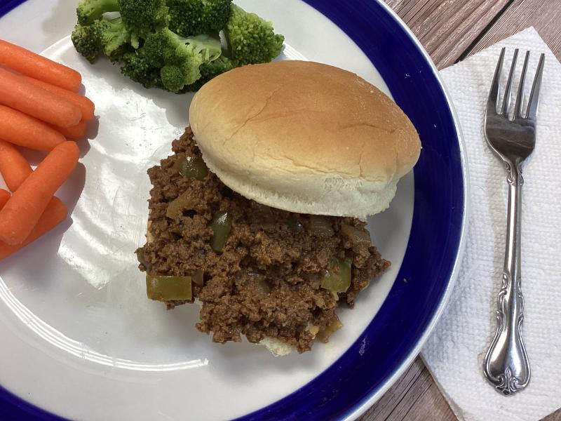 sloppy joe mix on bun plated with side of baby carrots and side of cooked broccoli