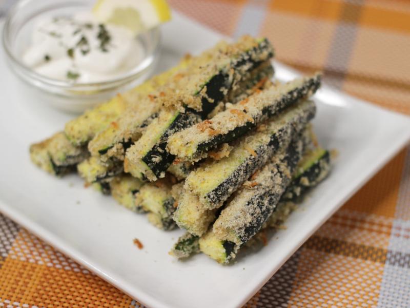 Breaded Zucchini Sticks on a white plate with a small container of dipping sauce