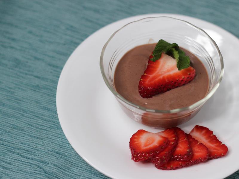 Small clear bowl with chocolate tofu pudding surrounded by sliced strawberries on a white plate.