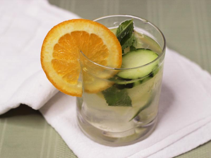 Glass of water with cucumber, mint and orange slices.