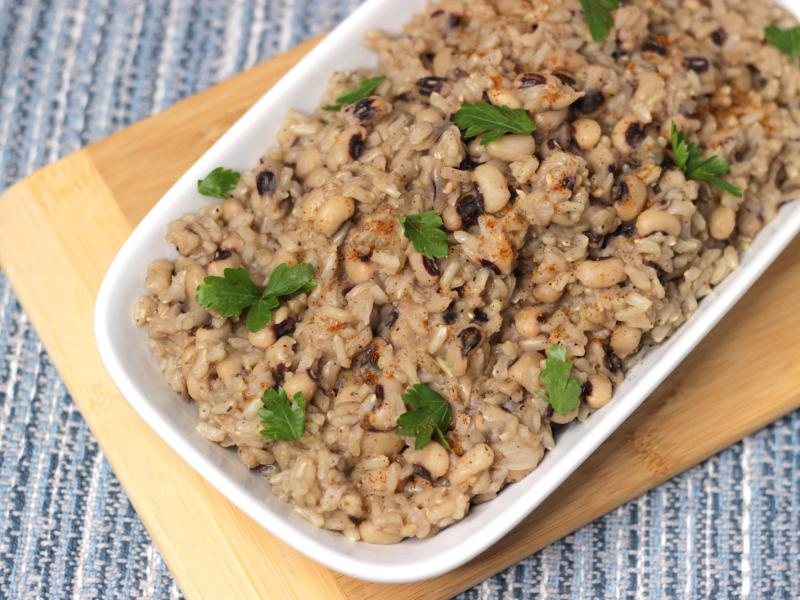 White bowl of Hoppin' John placed on a decorative wooden cutting board