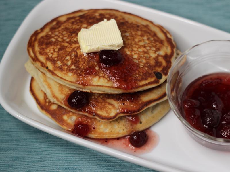 Three cranberry pancakes with a side of cranberry syrup