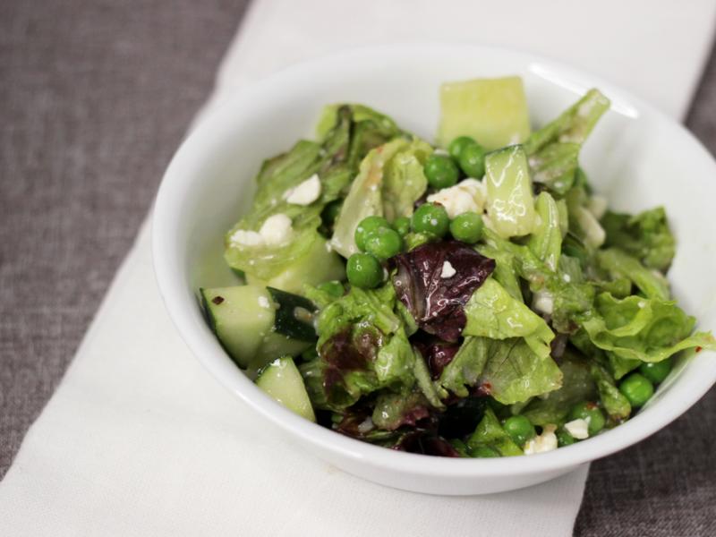 mixed salad greens with peas and feta. Served in a white bowl on a grey and white tablecloth