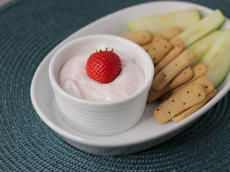 creamy strawberry dip in white bowl with graham crackers and apple on the side