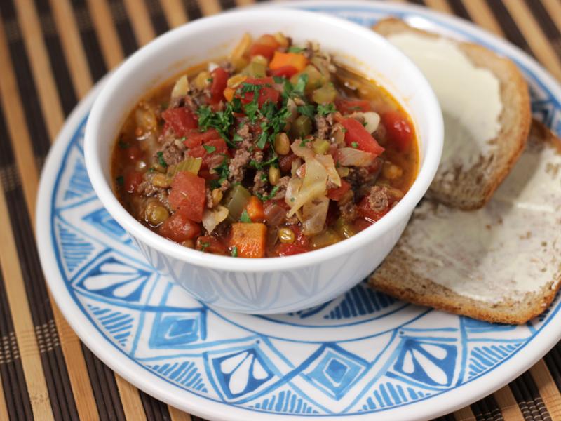 white bowl of venison cabbage lentil soup with buttered bread on the side