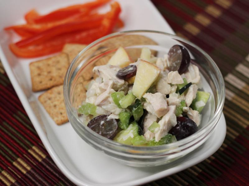 bowl of prepared crunchy chicken salad recipe served with sliced red peppers and wheat crackers on the side.