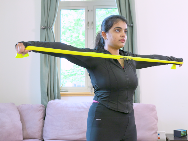 Person stretching an exercise band across chest with arms stretched out to each side.