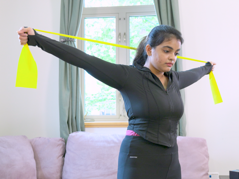 Person stretching an exercise band behind head with both arms stretched out to sides. 