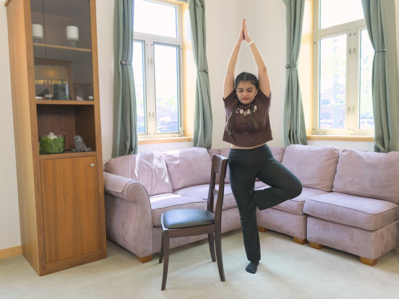woman practicing tree pose with a chair by her side for balance.