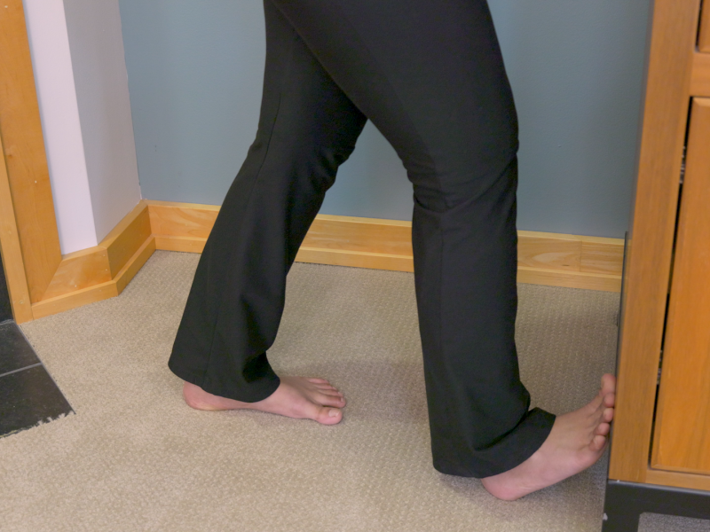Person with toes pressed against wall to stretch calf.