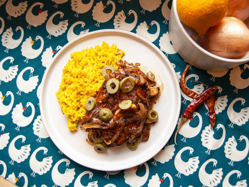 chicken yassa served on a white plate with side of yellow rice