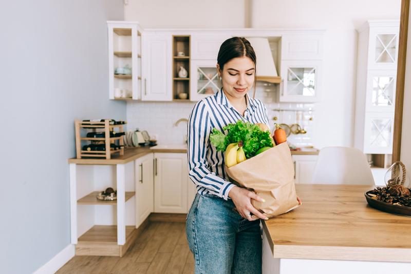 woman in kitchen putting groceries down on counter