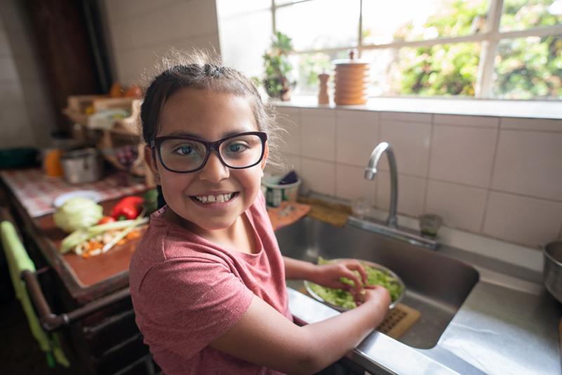 girl washing greens in sink