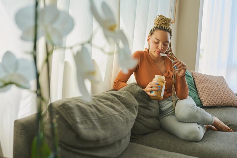 woman sitting on a couch and eating peanut butter with a spoon