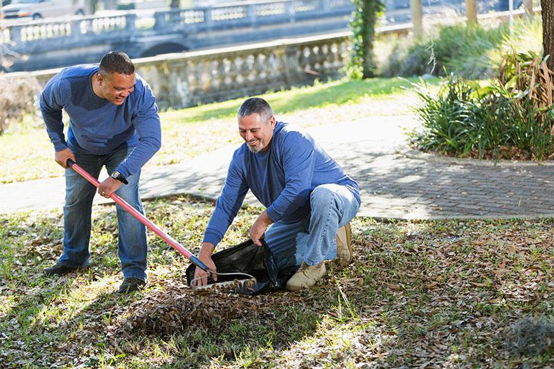 two men raking leaves, one holds open the bag