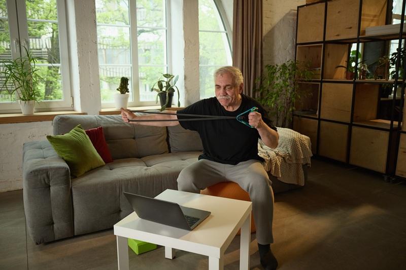 man sitting on chair in livingroom doing arm excercises with resistance band